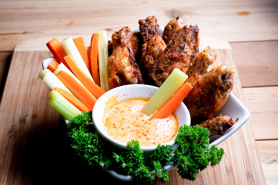 A dish with celery, carrot sticks, and chicken wings and a bowl of buffalo sauce.